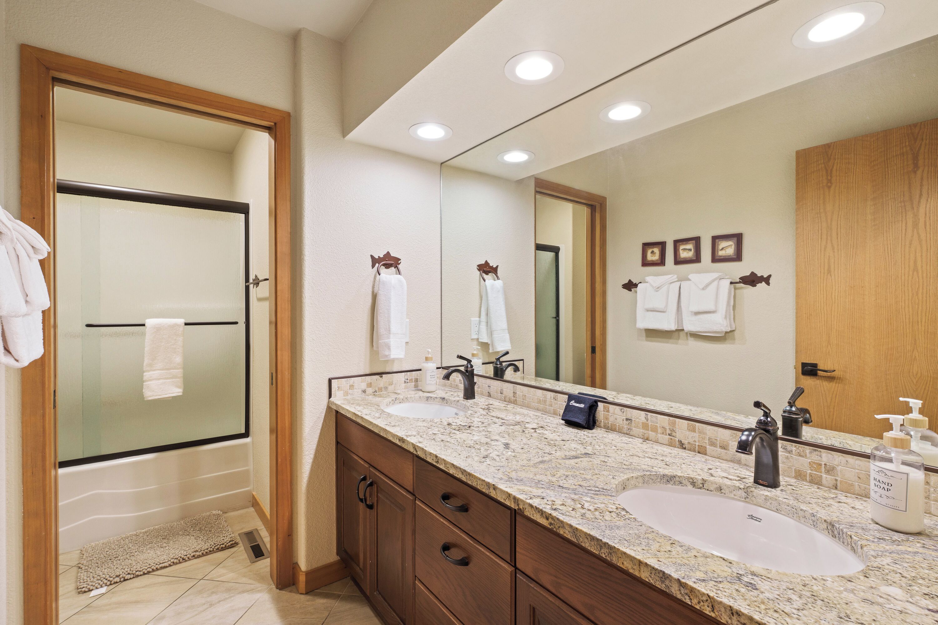 A bathroom with a large mirror, two sinks, a shower, and wooden cabinets.