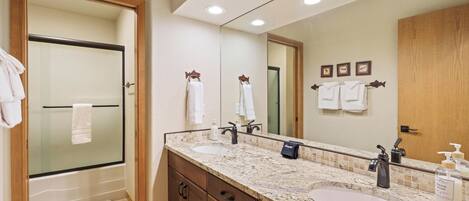 A bathroom with a large mirror, two sinks, a shower, and wooden cabinets.