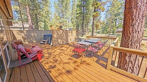 A wooden deck with outdoor furniture, a hot tub, and a view of a forest. - Tamarack 8 - Cute & Fun! Updated, SHARC, Bikes, Hot Tub (Sunriver)