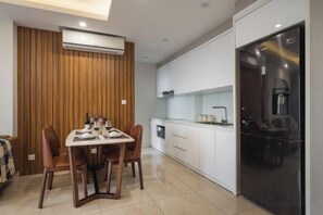 A modern kitchen with a refrigerator, white cabinets, and a dining area with a table and chairs. - Vinhomes D'Capitale - HANOIHOMES (Hanoi)