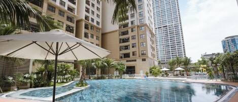 A swimming pool with lounge chairs and umbrellas, surrounded by tall buildings.