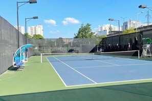An outdoor tennis court with a net, surrounded by a low wall and street lamps. - Vinhomes D'Capitale - HANOIHOMES (Hanoi)