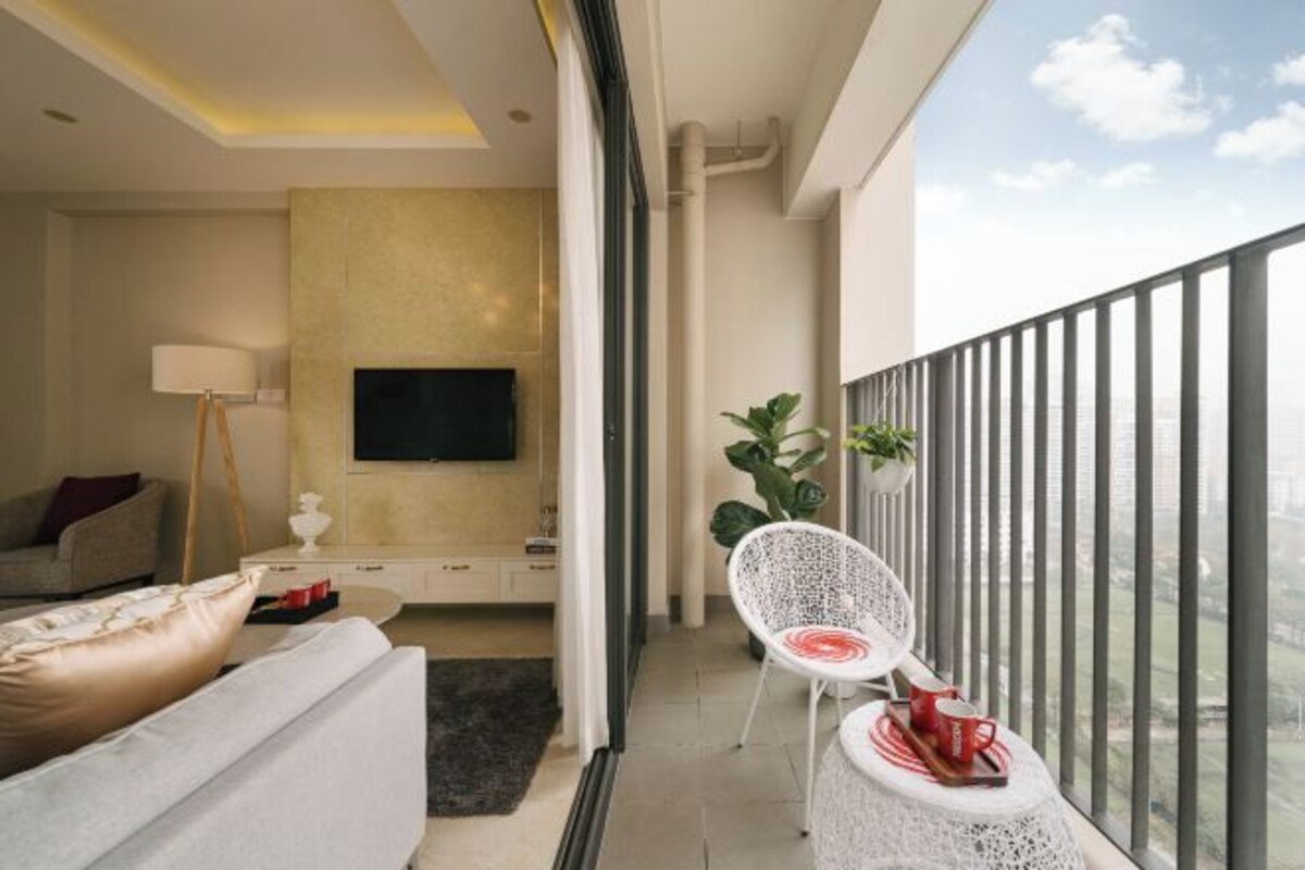 Una sala moderna con sofá, televisor de pantalla plana, comedor con una silla y mesa, y balcón con barandilla.
