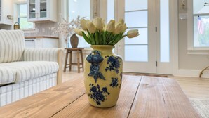 Una sala de estar con una mesa de centro de madera, un florero con flores, un sofá a rayas y una cocina al fondo.
