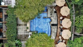 An aerial view of a hotel with a swimming pool surrounded by greenery, outdoor seating, and umbrellas.