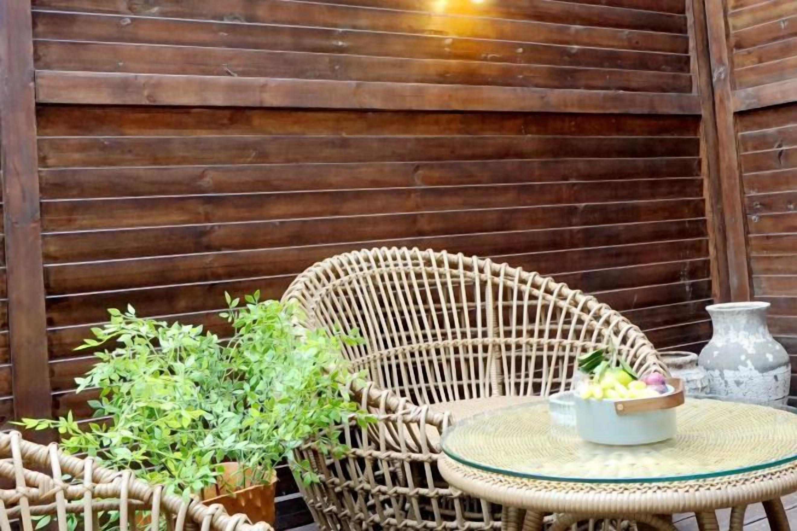 A wicker chair and a small round table with a bowl and a vase.