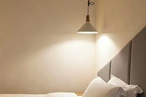 A bedroom with a bed, a hanging light fixture, and a sloped ceiling.