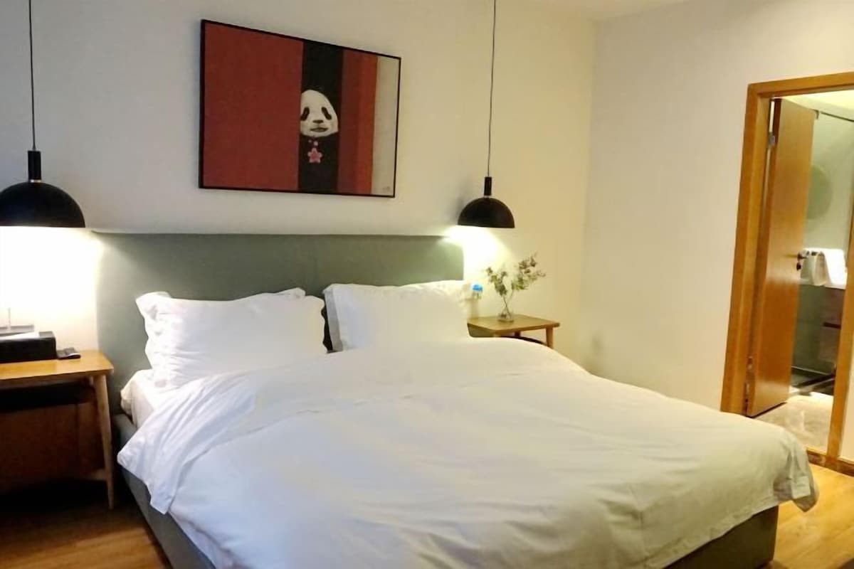 A neatly made bed with white linens, two bedside lamps, a small table with a vase, and a framed picture on the wall.