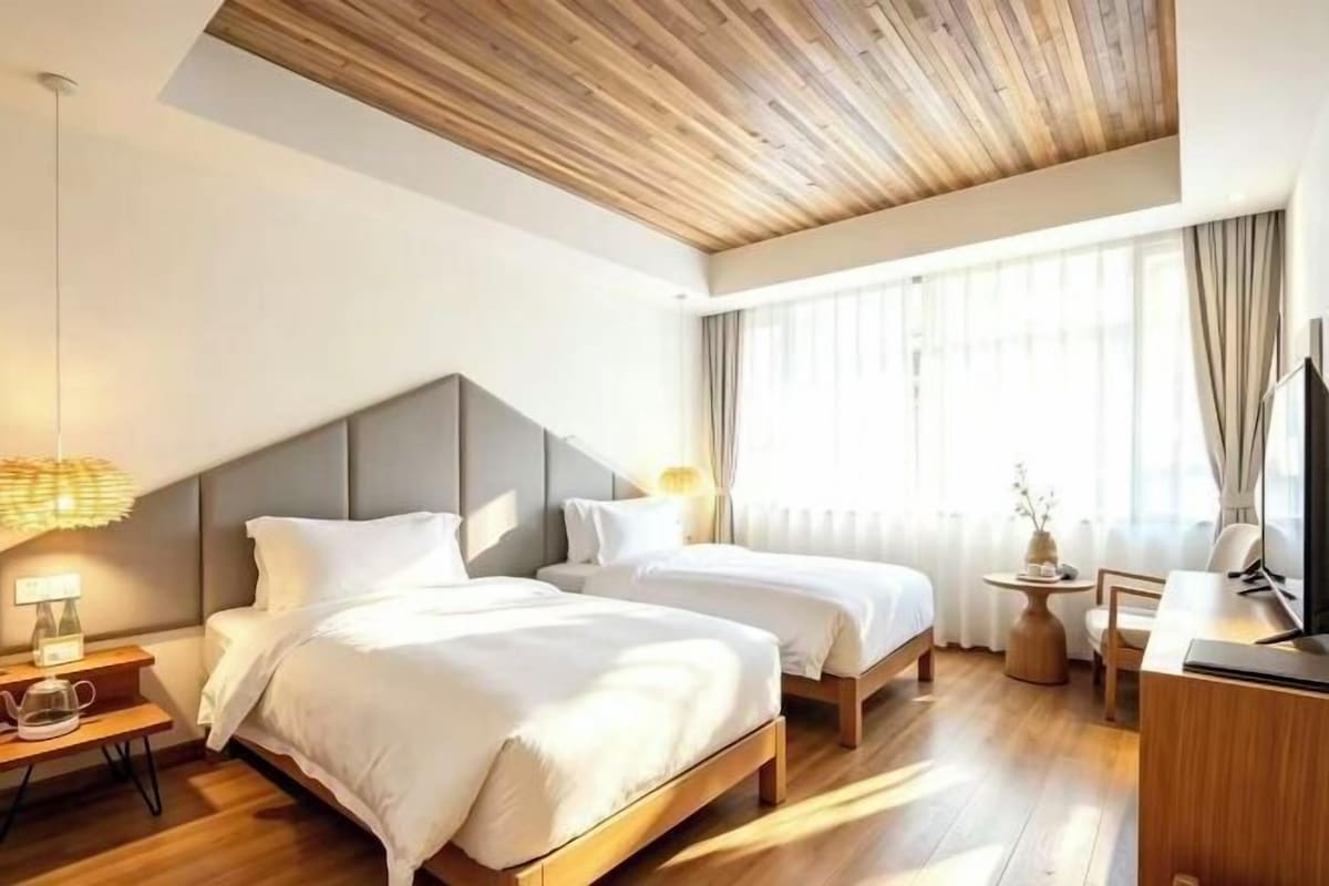 A hotel room with two beds, a wooden ceiling, a desk, and a television.