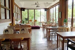 A spacious dining area with wooden tables and chairs, large windows, and a ceiling fan.