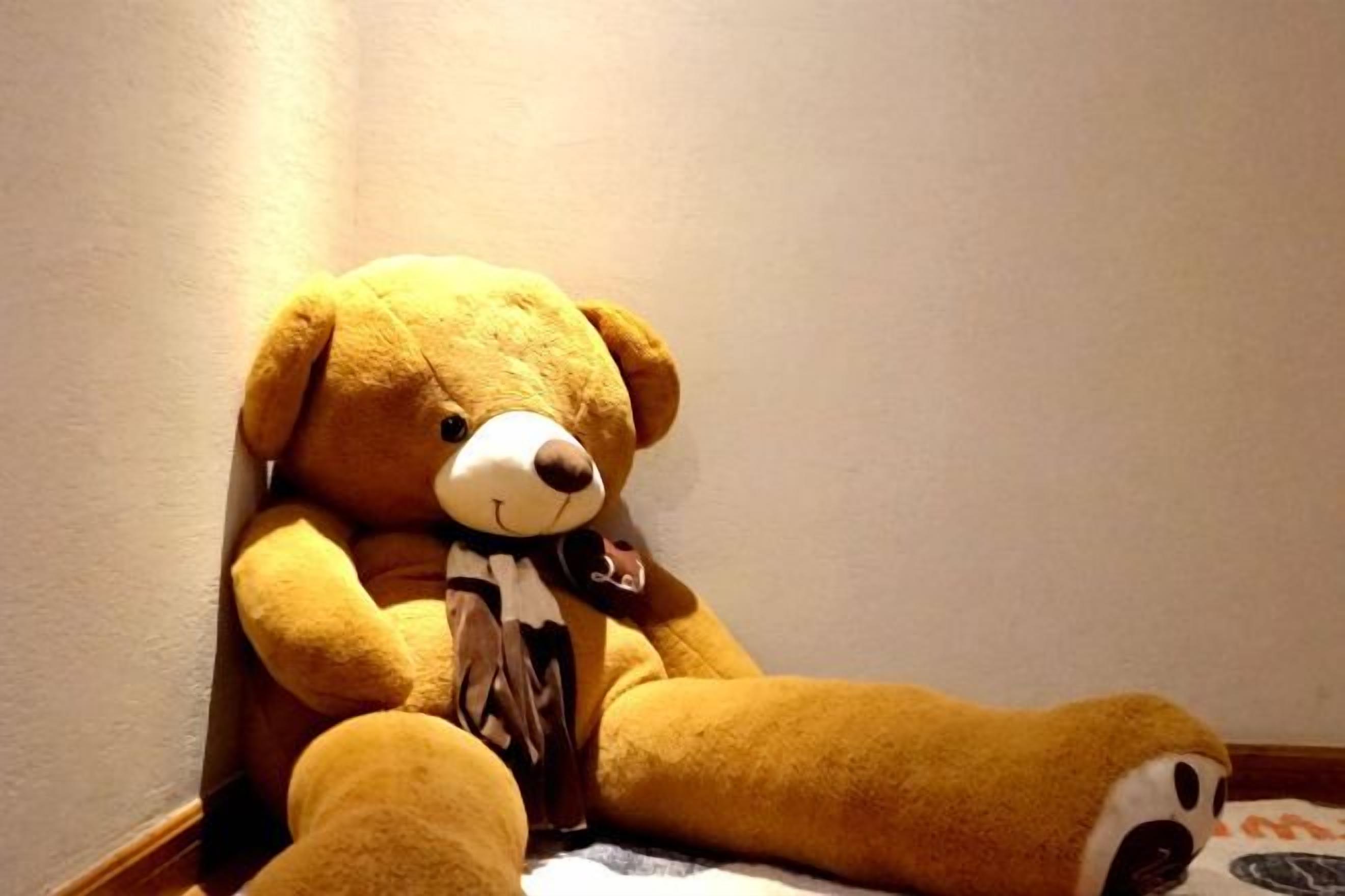 A large teddy bear sitting against a wall in a corner.