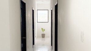 Un long couloir étroit aux murs blancs et aux portes noires, qui mène à un tableau encadré accroché au fond.