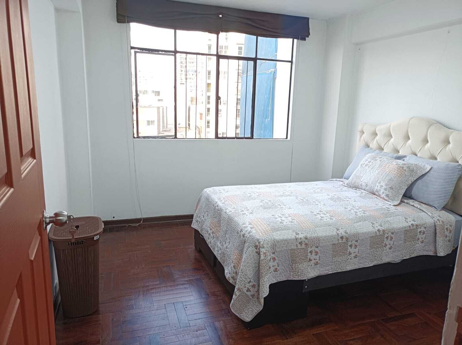 Una camera da letto con un letto, una finestra, una porta e un cestino.