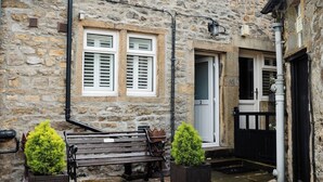 A stone building with two windows, a bench, and two potted plants. - Cottage in Grassington: Cosy 2-Bedroom Retreat (Grassington)