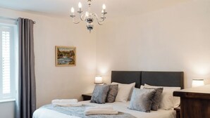 A neatly arranged bedroom with a large bed, bedside lamps, a chandelier, and a painting on the wall. - Cottage in Grassington: Cosy 2-Bedroom Retreat (Grassington)