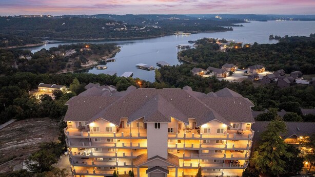 Um hotel com vários andares e um pátio central, rodeado por um lago e colinas florestadas.