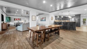 Uma cozinha ampla com uma mesa de madeira e banquetas, uma sala de jantar com sofá e uma sala de estar com uma planta grande e obras de arte.