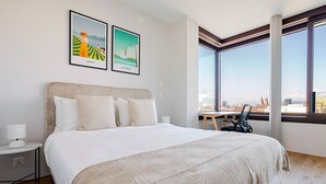 A modern hotel room with a large bed, a desk, and a view of a cityscape through large windows. - Blueground | Basel-Vorstaedte, view, nr Kunstmuseum (Basel)