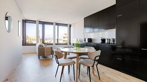A modern kitchen with black cabinets, a dining table with chairs, and large windows offering a city view. - Blueground | Basel-Vorstaedte, view, nr Kunstmuseum (Basel)