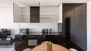 A modern kitchen with black cabinets, a built-in oven, a coffee maker, and a dining table with chairs. - Blueground | Basel-Vorstaedte, view, nr Kunstmuseum (Basel)