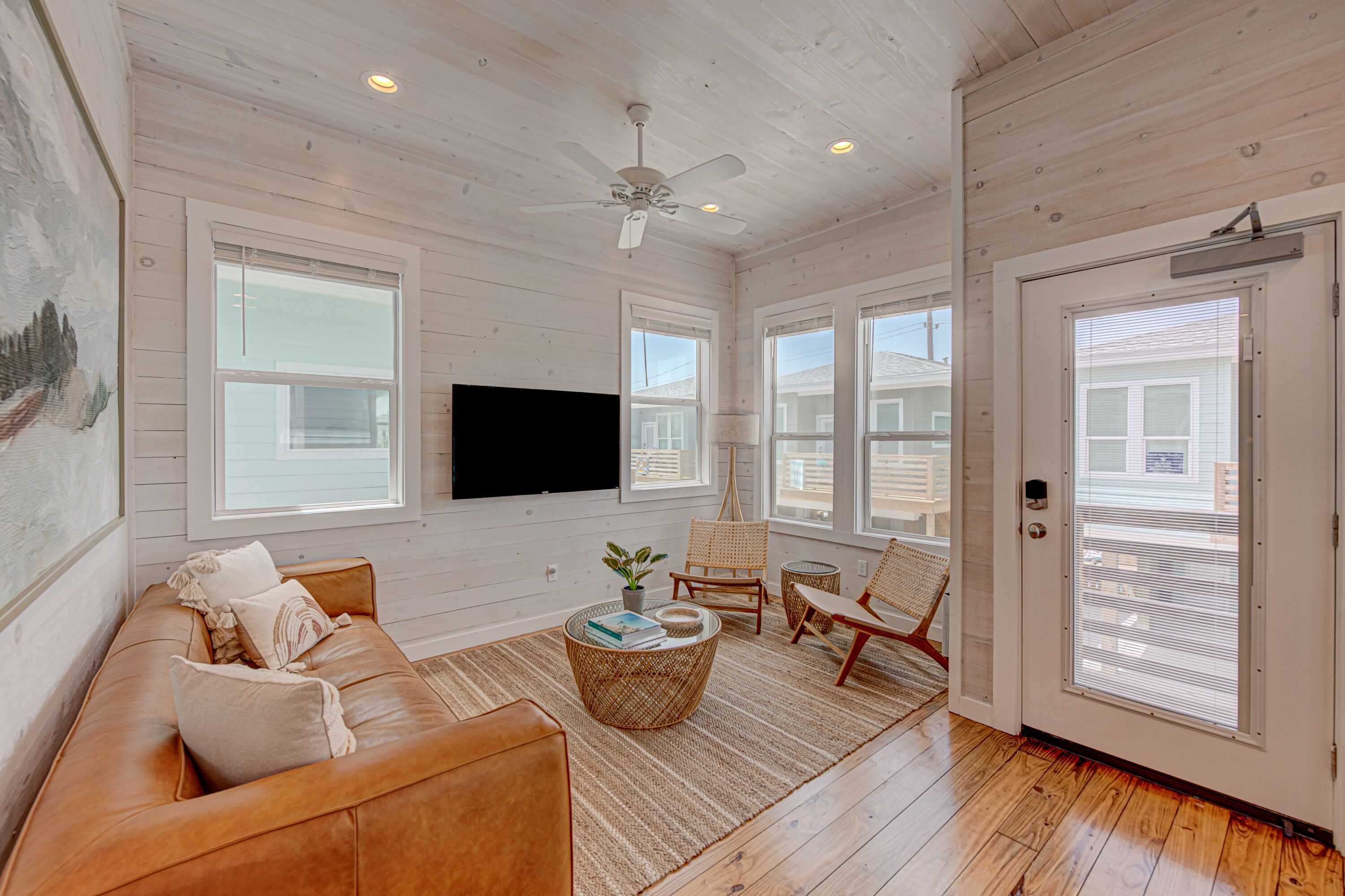 A spacious living room with a leather sofa, a flat-screen TV mounted on the wall, and a ceiling fan.