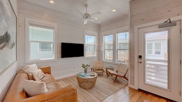 A spacious living room with a leather sofa, a flat-screen TV mounted on the wall, and a ceiling fan.