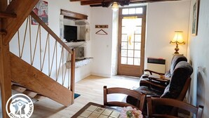Ein rustikales Interieur mit einer Holztreppe, einem Fernseher auf einem Steinsims, einem Esstisch mit Stühlen und einer Lampe.