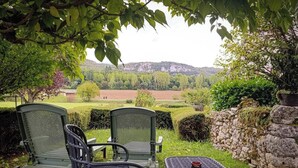Blick auf eine ländliche Landschaft mit einer Steinmauer, einem kleinen Tisch mit Tasse und zwei Stühlen.