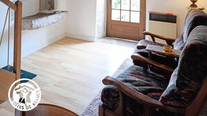 Ein gemütliches Wohnzimmer mit Kamin aus Stein, Holzbalken, Fernseher, einer Couch und einer Lampe.