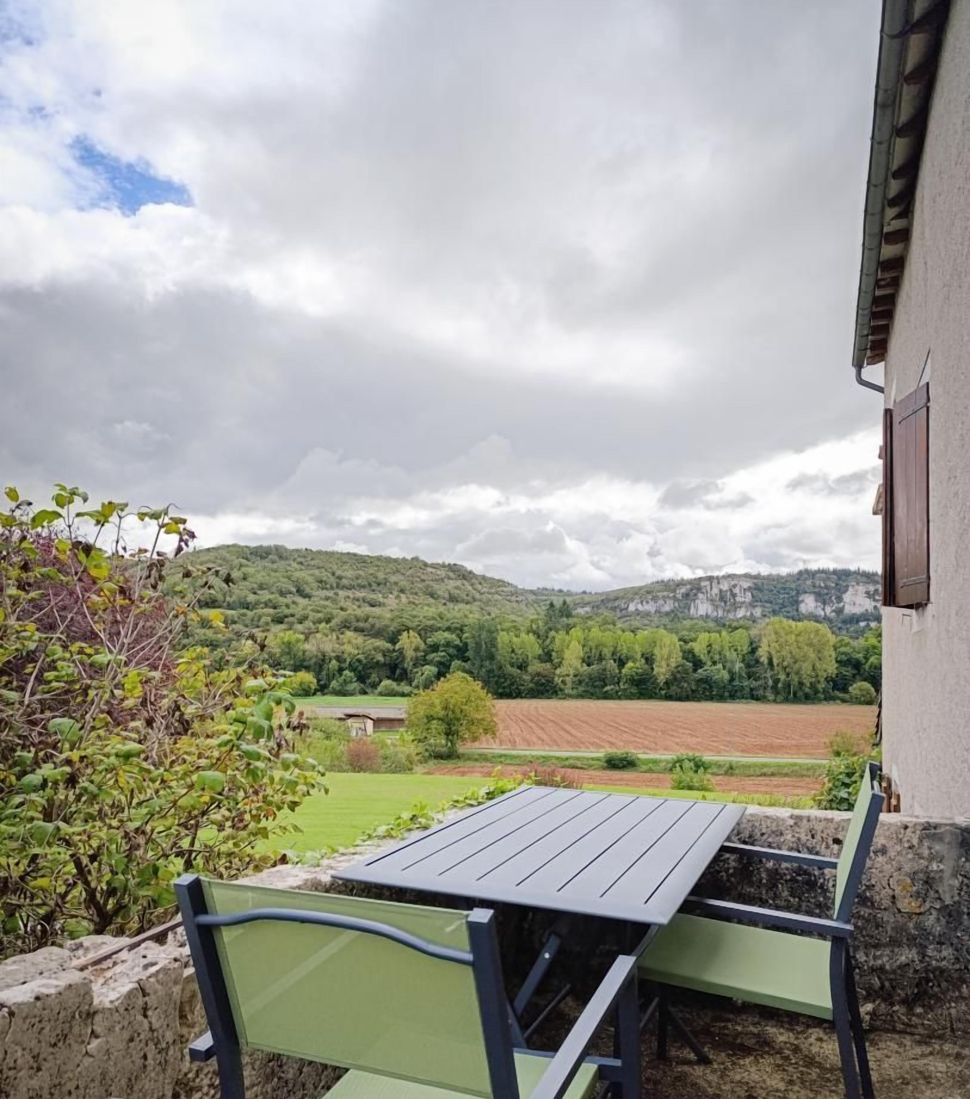A patio with a table and chairs overlooking a rural landscape with fields and hills.