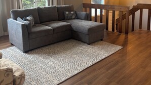 A living room with a grey sectional sofa, a patterned rug, wooden flooring, a staircase, and a chandelier. - Relaxing-Retreat, Anchorage Getaway, Cozy & Newly Remodeled (Anchorage)
