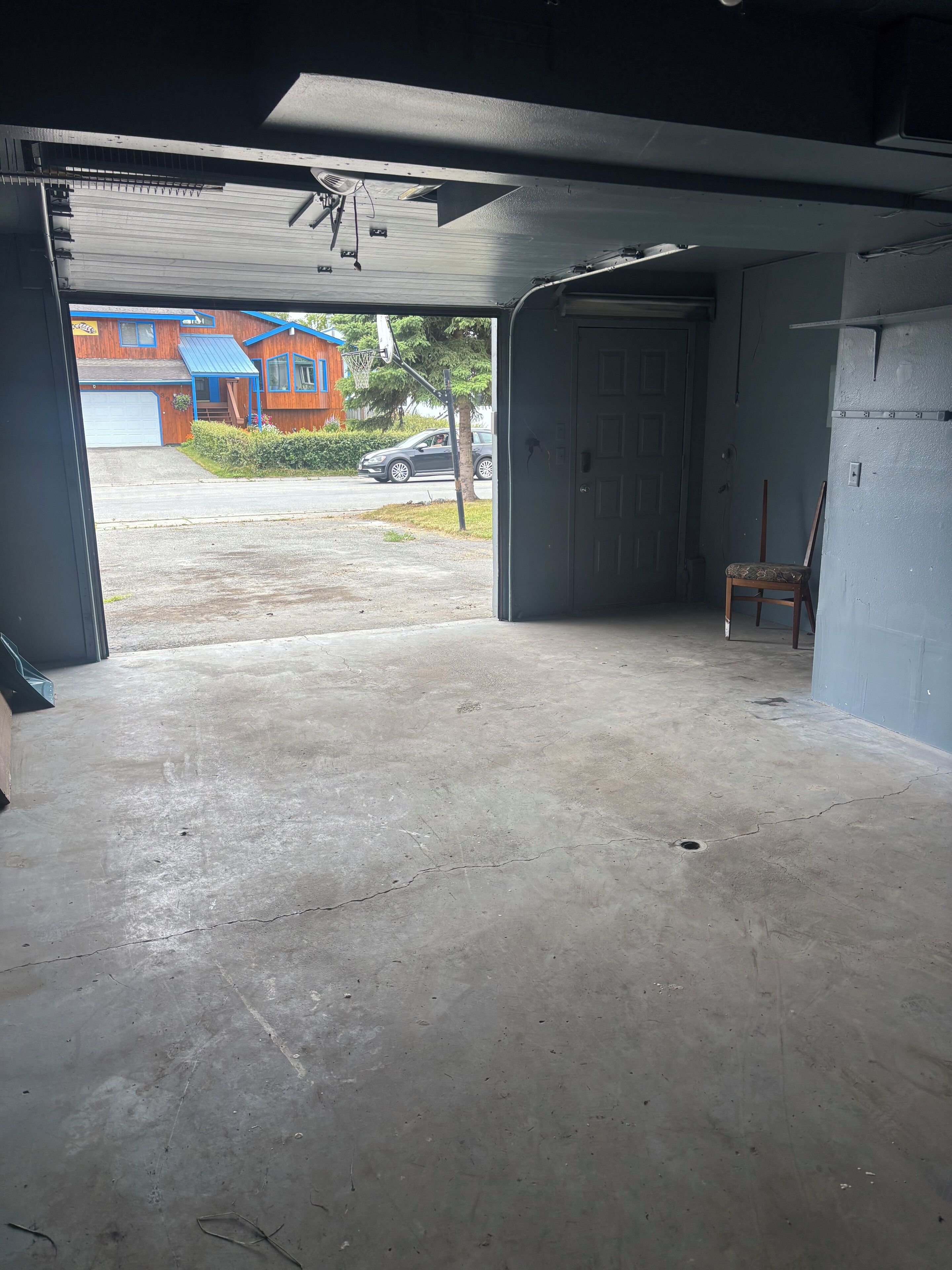 Eine offene Garage mit Betonboden, einem Holzstuhl und einer blauen Wand.
