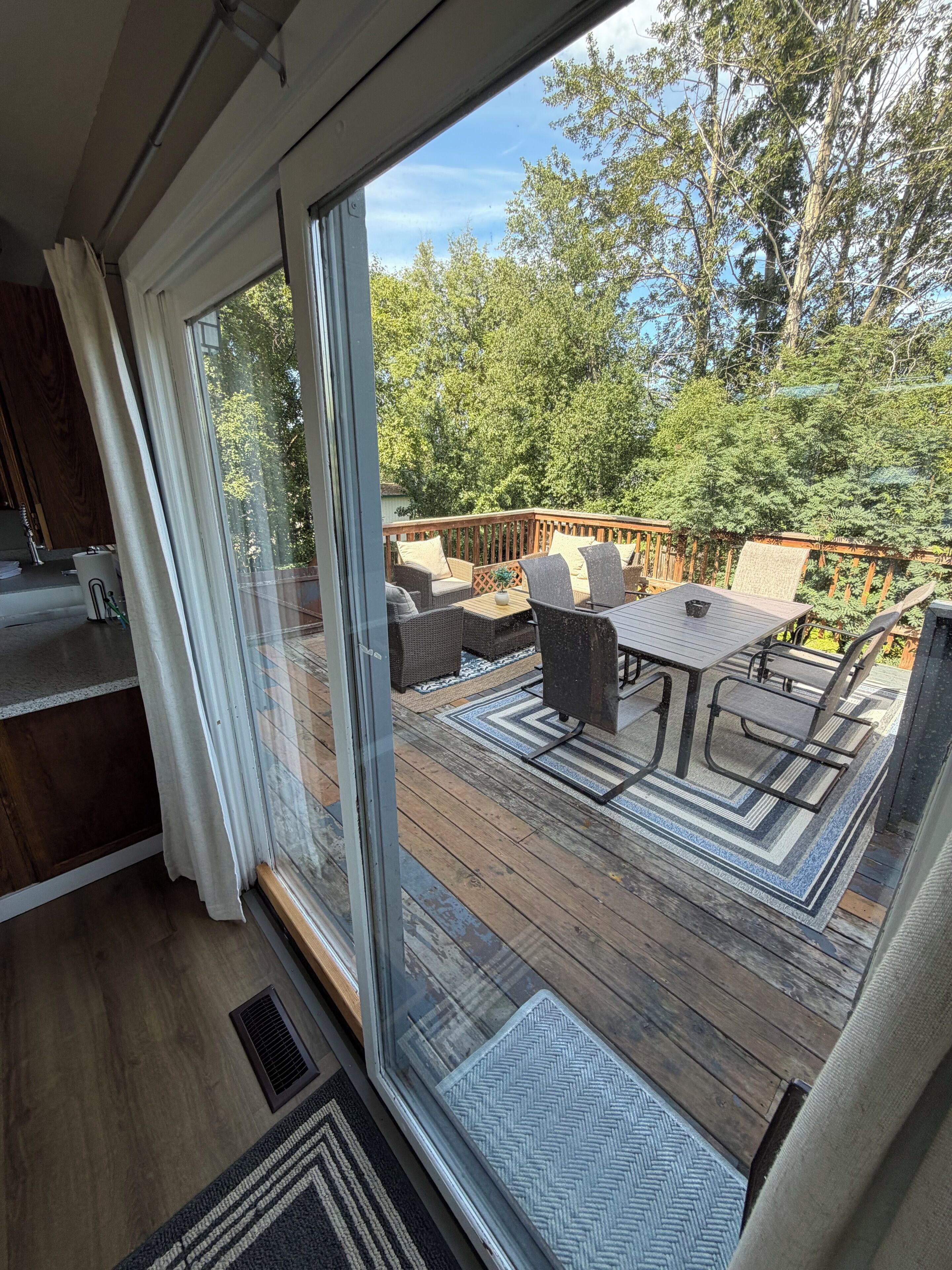 Una terraza con mobiliario exterior, vista a árboles y cielo despejado.