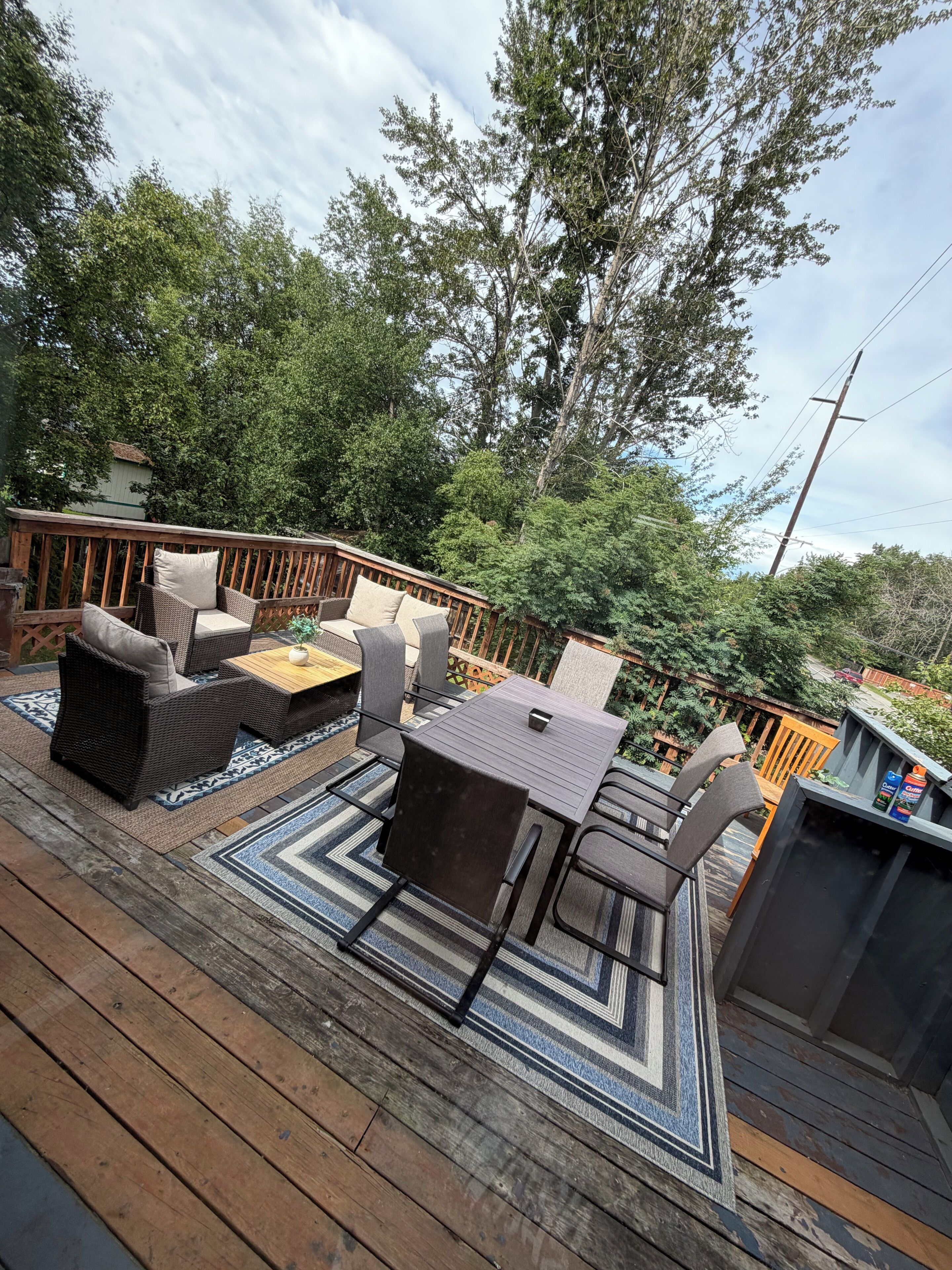 A deck with outdoor furniture, including a table and chairs, surrounded by a wooden deck and a patterned rug.