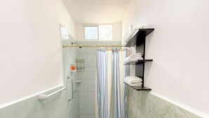 A narrow bathroom with a shower, toilet, and a bench.