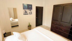 A bedroom with a large bed, a wardrobe, a mirror, and artwork on the wall.