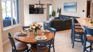 A dining area with a round table, chairs, a vase of flowers, a TV, a sofa, and a painting on the wall. - 4BR family home w/ pool & lanai (Lakeland)