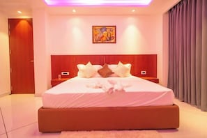 Un dormitorio moderno con una cama grande, cabecera, mesita de noche, una obra de arte colgada en la pared y una ventana con cortinas.