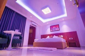 A modern hotel room with a large bed, a round table, and a ceiling light fixture. - J60 Suites, Ashok Vihar - Near Netaji Subhash Place (North West Delhi)