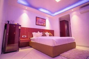 A bedroom with a bed, a wardrobe, a nightstand, a painting, and a door. - J60 Suites, Ashok Vihar - Near Netaji Subhash Place (North West Delhi)