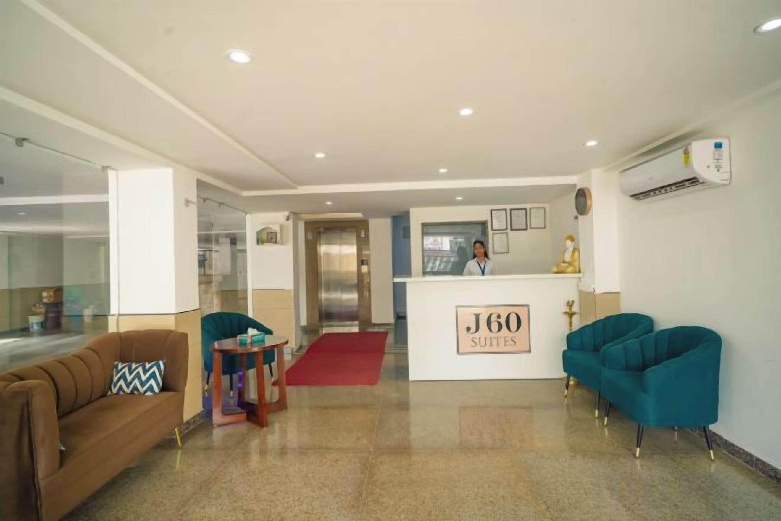 Uma área de recepção de hotel, com balcão, recepcionista e um tapete vermelho que leva à entrada.
