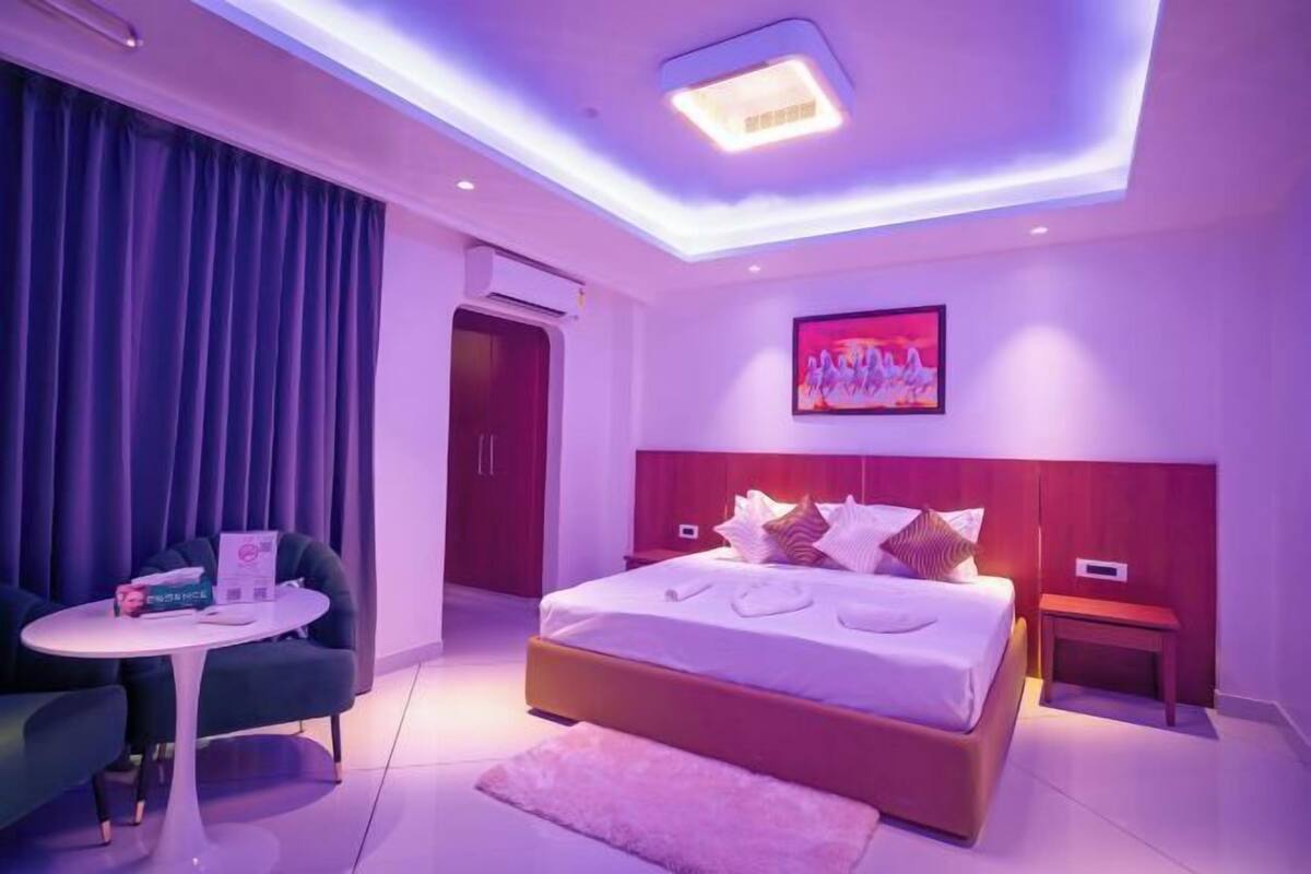 A modern bedroom with a bed, a small table, a chair, and a painting on the wall.