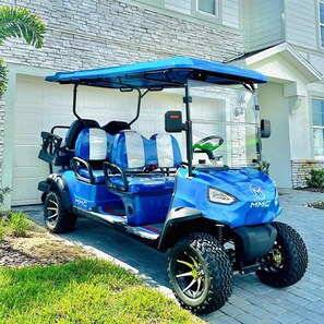 A golf cart with 'MMC' branding parked in front of a house.