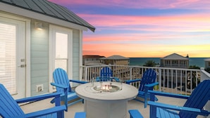 A balcony with blue Adirondack chairs, a fire pit, and a view of the ocean at sunset. - 🌅 Chasing Sunsets | Harbor + Gulf Views | FREE Parasailing ☀️ (Destin)