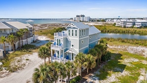 A large, two-story beachfront house with a balcony, surrounded by palm trees and a beach. - 🌅 Chasing Sunsets | Harbor + Gulf Views | FREE Parasailing ☀️ (Destin)