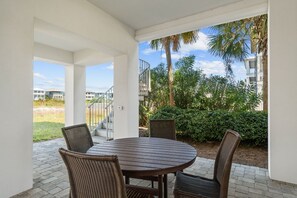 A covered patio with a round table and four wicker chairs, overlooking a landscaped garden and a residential area. - 🌅 Chasing Sunsets | Harbor + Gulf Views | FREE Parasailing ☀️ (Destin)