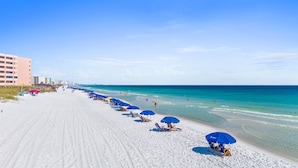 A beach with rows of blue umbrellas and beach chairs, a sandy shore, and a clear blue sky. - 🌅 Chasing Sunsets | Harbor + Gulf Views | FREE Parasailing ☀️ (Destin)