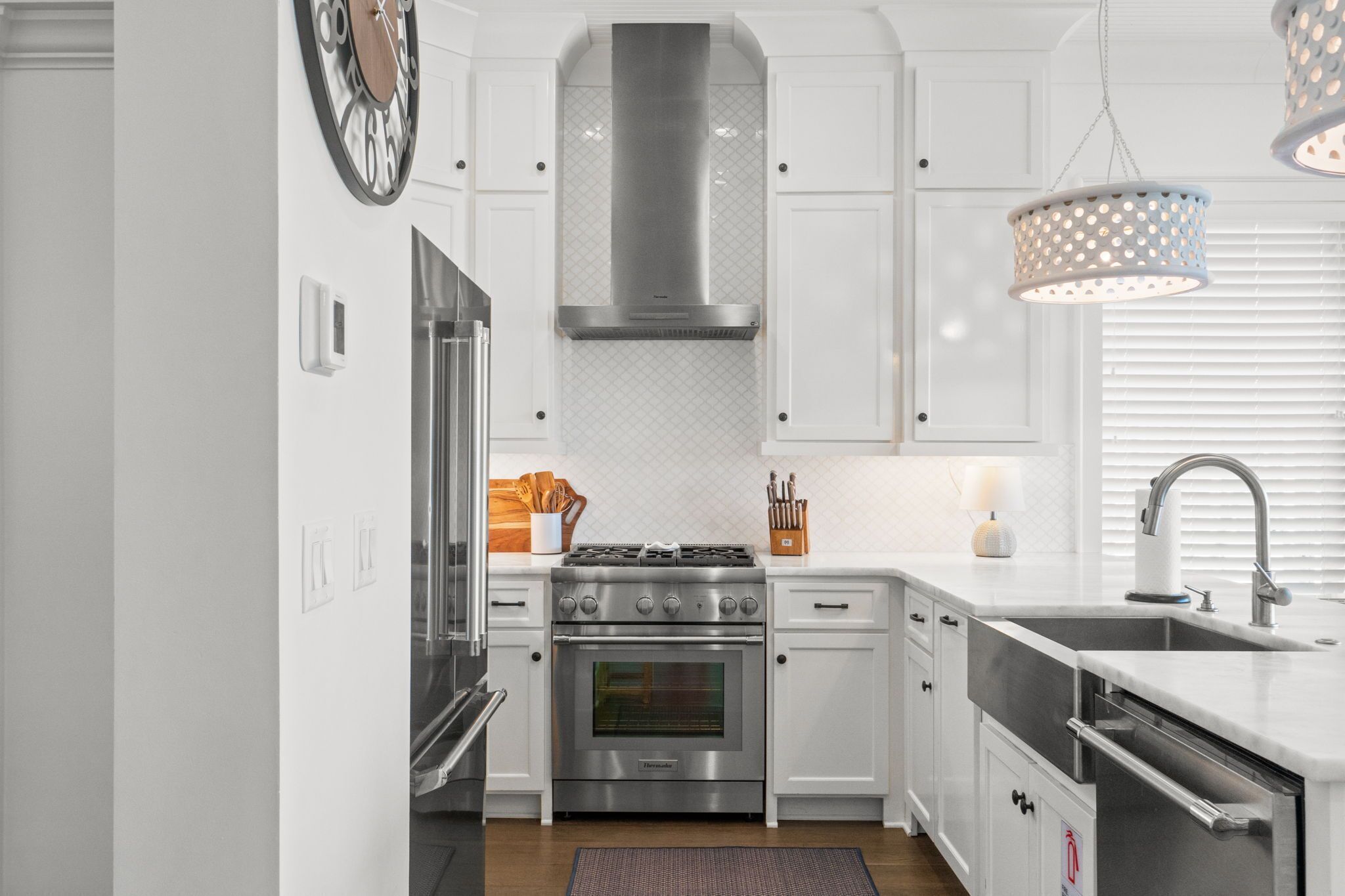 A modern kitchen with white cabinetry, stainless steel appliances, a built-in oven, and a hanging light fixture.