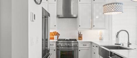 A modern kitchen with white cabinetry, stainless steel appliances, a built-in oven, and a hanging light fixture.