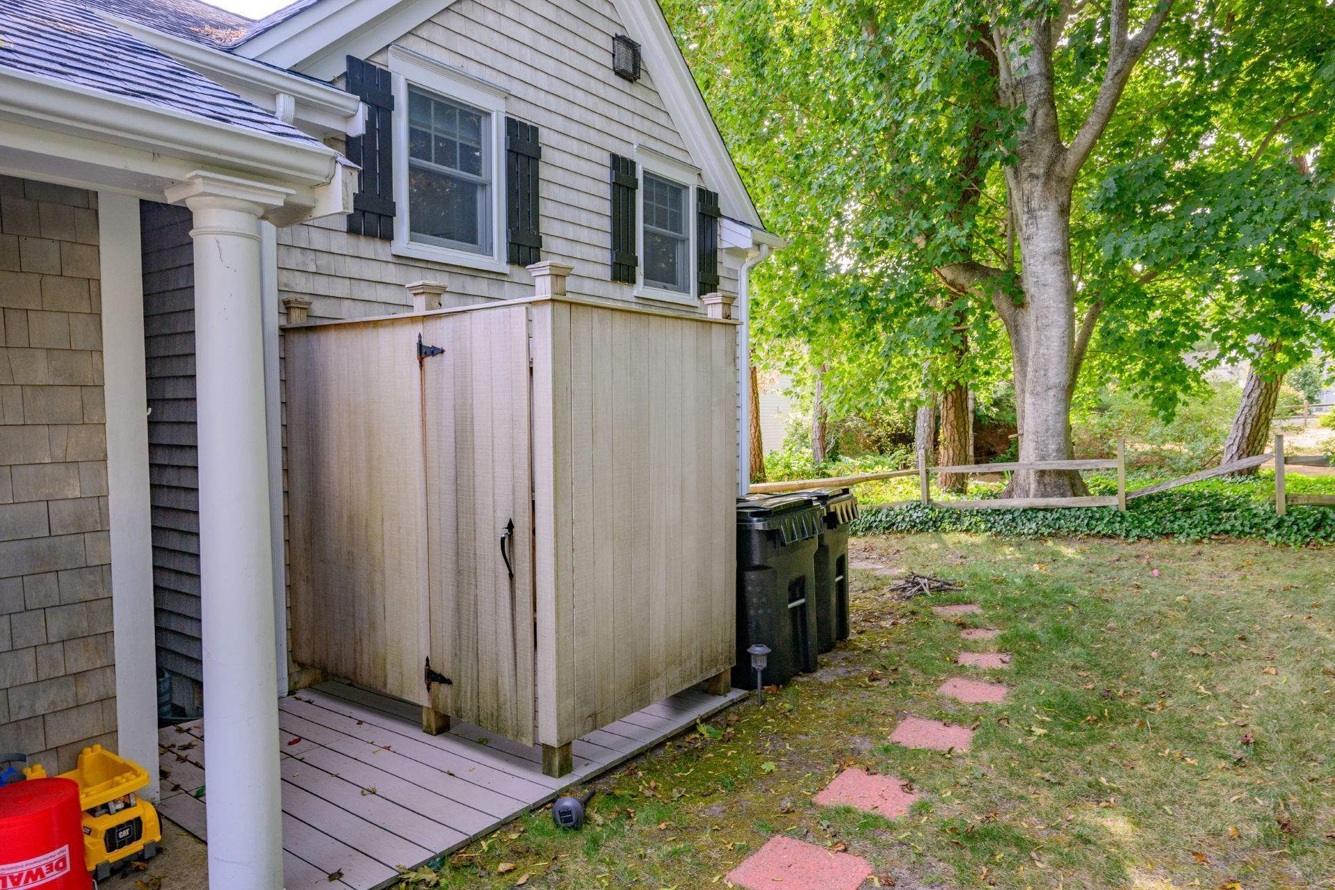 A wooden shed with a porch, a tree, and a fence in a backyard.